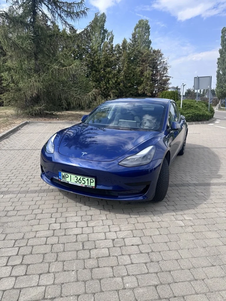 Niebieska Tesla Model 3 – ujęcie przodu na parkingu w dzień